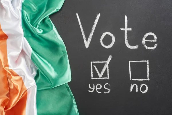 Top view of white vote lettering and check mark near yes word on black chalkboard near flag of Ireland — Stock Photo