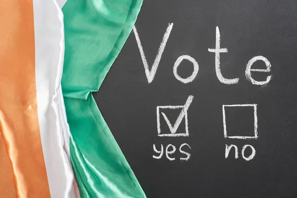 Top view of vote lettering and check mark near yes word on black chalkboard near flag of Ireland — стоковое фото