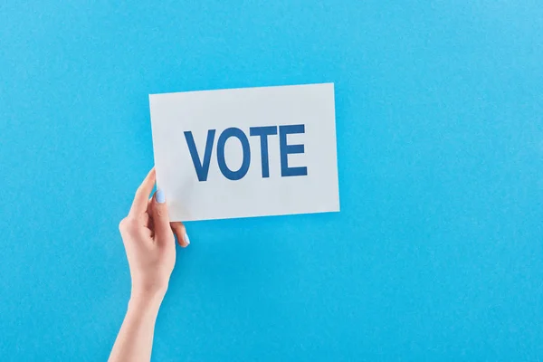 Vue partielle de la femme tenant une carte blanche avec lettrage de vote sur fond bleu — Photo de stock