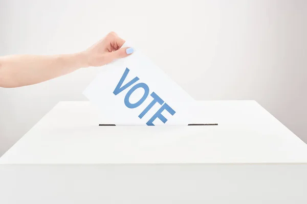 Vista parcial de la mujer poniendo el voto en caja sobre fondo gris - foto de stock