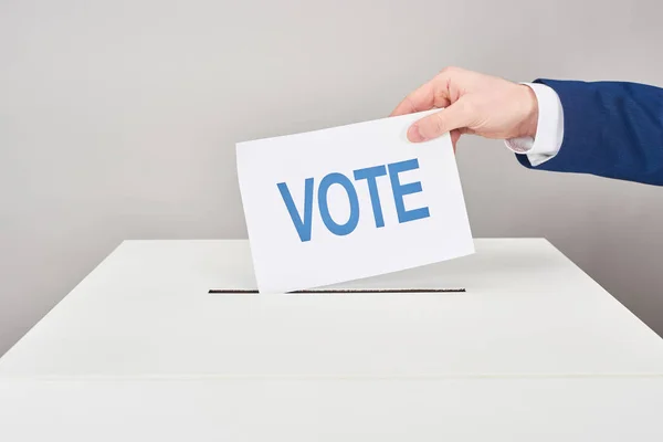 Vue recadrée de l'homme mettant le vote en boîte sur fond gris — Photo de stock