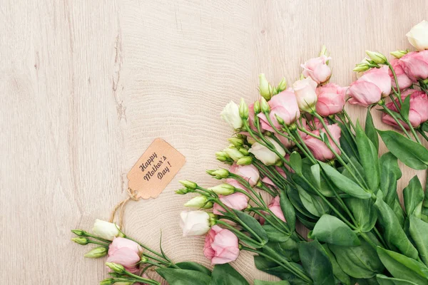 Top view of eustoma flowers with happy mothers day paper label on wooden table with copy space — Stock Photo