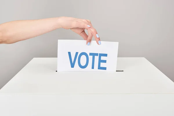 Vista parcial de la mujer poniendo tarjeta con voto en caja aislado en gris - foto de stock