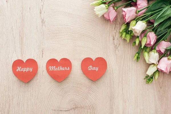 Вид зверху на листівки у формі серця з щасливими матерями, що пишуть день і квіти еустоми на дерев'яному столі — стокове фото