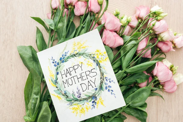 Вид зверху на рожеві квіти еустоми і листівка з щасливими матерями день написання на столі — стокове фото