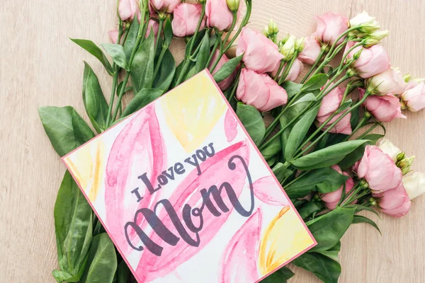 Vista superior de flores eustoma e cartão com eu amo sua mãe na mesa de madeira — Fotografia de Stock