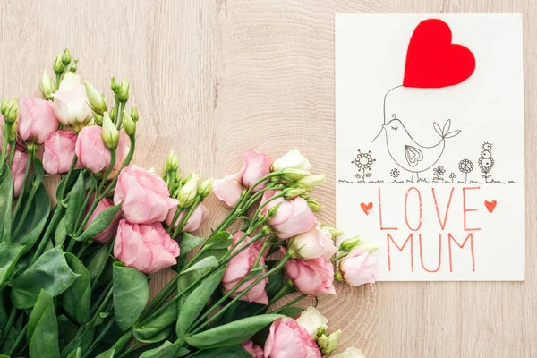 Вид зверху на рожеві квіти еустоми і листівка з любов'ю слова мами на дерев'яному столі — стокове фото