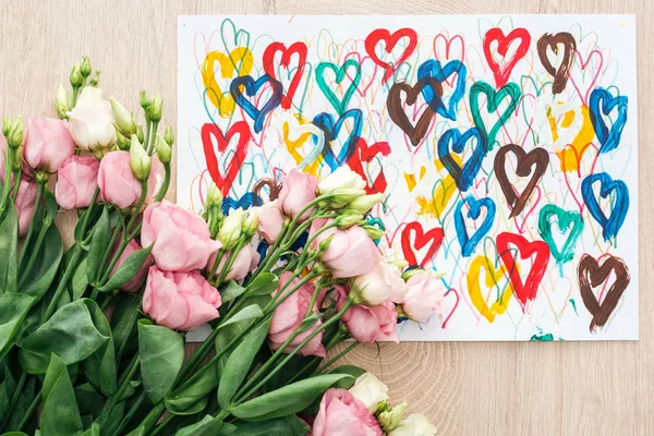 Top view of bouquet with eustoma flowers and drawing with colorful hearts on wooden table — Stock Photo