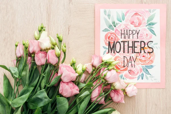 Draufsicht auf rosa Eustoma-Blumen und Karte mit glücklichem Muttertag-Schriftzug auf Tisch — Stockfoto