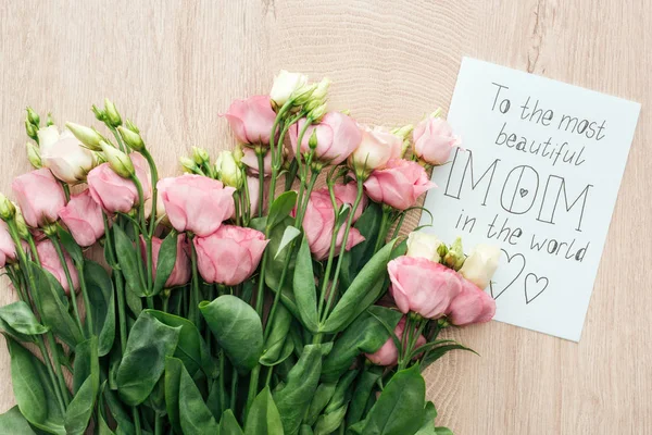 Top view of pink eustoma flowers and card with to the most beautiful mom in the world words on wooden table — Stock Photo