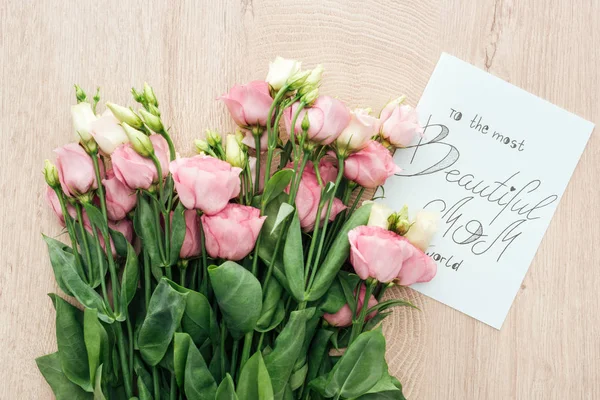 Vista superior de flores eustoma rosa e cartão com a mãe mais bonita do mundo lettering na mesa de madeira — Fotografia de Stock