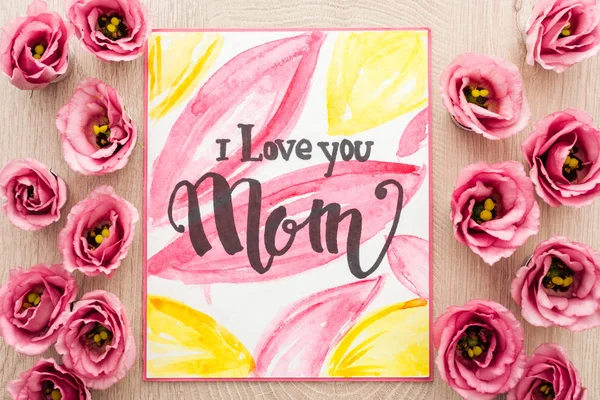Vista superior de flores eustoma y tarjeta con te amo mamá palabras en mesa de madera - foto de stock