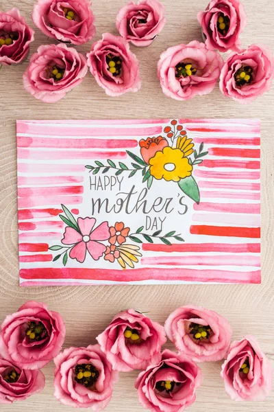 Top view of eustoma flowers and card with happy mothers day writing on wooden surface — Stock Photo