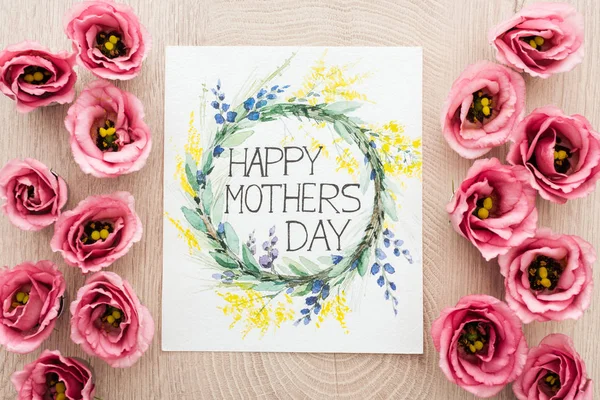 Vista superior de flores eustoma y tarjeta con feliz día de las madres escritura en la superficie de madera - foto de stock