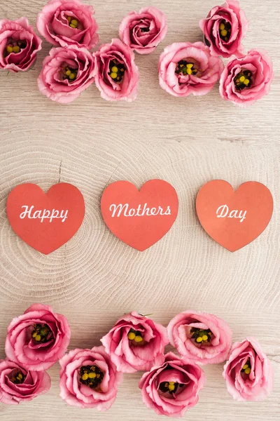 Vue du dessus des cartes en forme de coeur avec l'écriture heureuse de la fête des mères et les fleurs d'eustomie sur la table en bois — Photo de stock