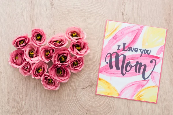 Top view of heart sign made of eustoma flowers and card with i love you mom lettering on wooden surface — Stock Photo