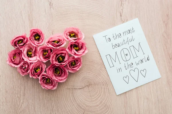 Vista superior do sinal do coração feito de flores de eustoma e cartão com a mãe mais bonita do mundo lettering na mesa de madeira — Fotografia de Stock