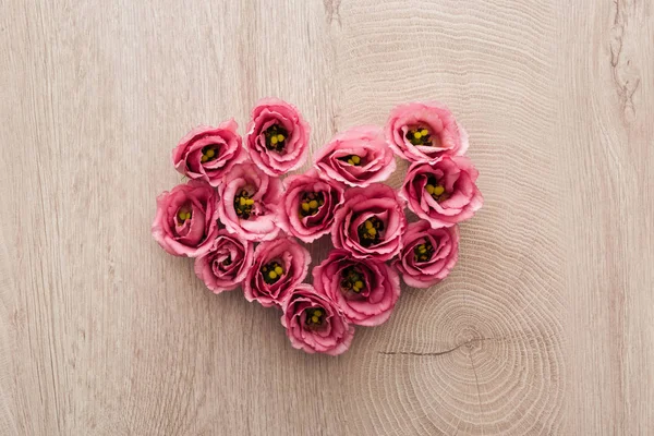 Vue du dessus du signe du coeur en fleurs d'eustomes roses sur une table en bois — Photo de stock