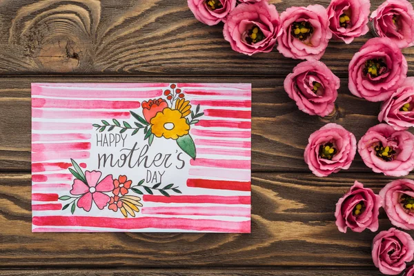 Vue du dessus des fleurs d'eustomie et carte avec salutation heureuse de la fête des mères sur la surface en bois — Photo de stock
