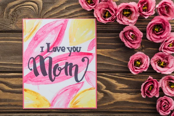 Vista superior de flores eustoma e cartão com eu amo você mãe lettering na mesa de madeira — Fotografia de Stock
