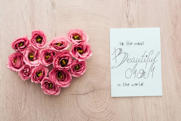 Vista dall'alto del segno del cuore fatto di fiori di eustoma e carta con alla mamma più bella del mondo lettering su superficie di legno — Foto stock