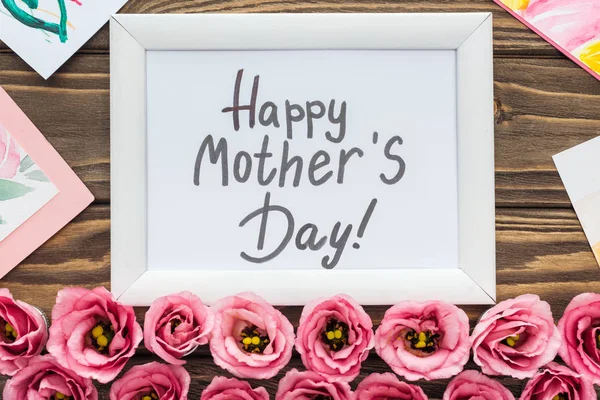 Top view of cards, frame with happy mothers day lettering and pink eustoma flowers on wooden table — Stock Photo