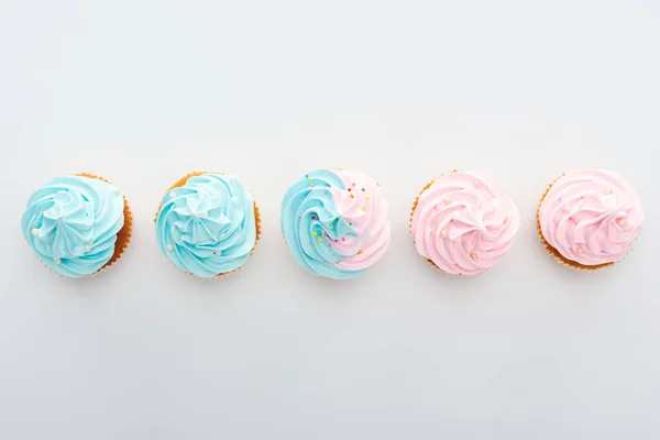 Vue de dessus des cupcakes colorés savoureux avec des saupoudres en rangée isolé sur blanc — Photo de stock