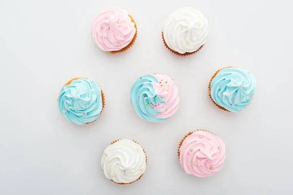 Vista superior de deliciosos cupcakes blancos, rosados y azules con aspersiones aisladas en blanco - foto de stock