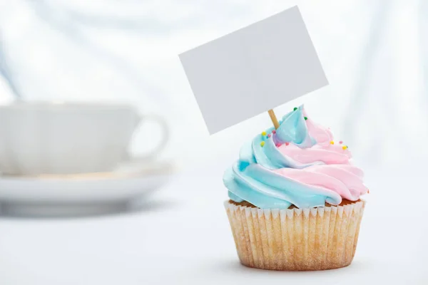 Enfoque selectivo de cupcake sabroso decorado con aspersiones y tarjeta en blanco - foto de stock