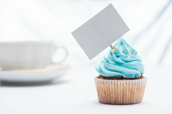 Foco selectivo de delicioso cupcake azul decorado con aspersiones y tarjeta en blanco - foto de stock