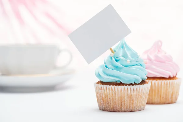 Enfoque selectivo de sabrosos cupcakes decorados con aspersiones y tarjeta en blanco - foto de stock