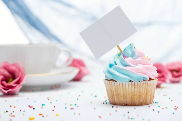 Foco selectivo de delicioso cupcake decorado con aspersiones y tarjeta en blanco - foto de stock