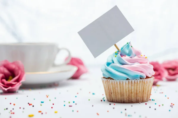 Foco selectivo de delicioso cupcake decorado con aspersiones y tarjeta en blanco - foto de stock