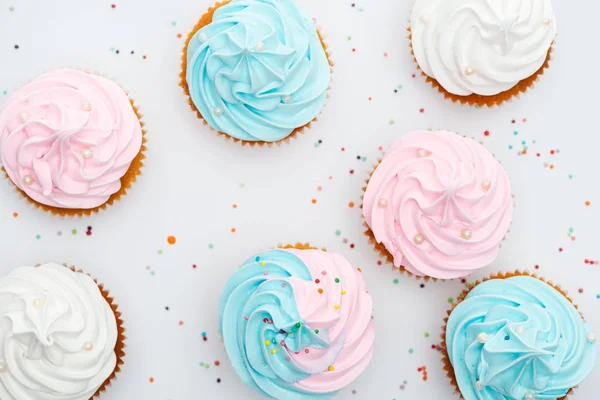 Vista superior de deliciosos cupcakes brancos, rosa e azul com polvilhas isoladas em branco — Fotografia de Stock