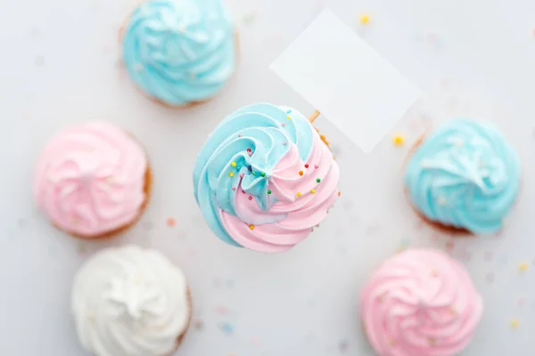 Vista superior de deliciosos cupcakes de color rosa, blanco y azul con aspersiones y tarjeta en blanco aislado en blanco - foto de stock