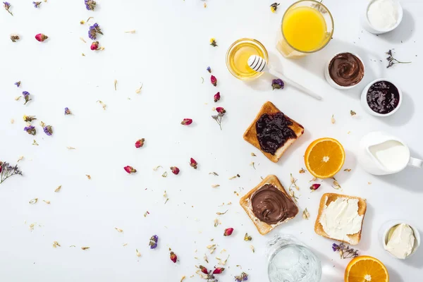 Vue de dessus des toasts savoureux, bols avec confiture et oranges près des verres d'eau et jus d'orange sur blanc — Photo de stock