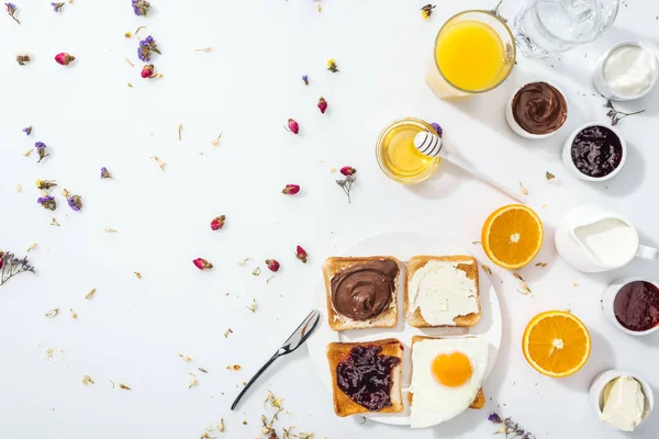 Вид зверху тарілки з тостами, варенням та смаженим яйцем біля склянок води та апельсиновим соком на білому — стокове фото
