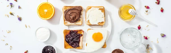 Panoramic shot of tasty toasts with jam, cream cheese, chocolate cream and friend egg on white — Stock Photo