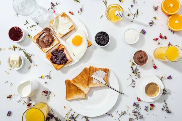 Вид сверху на тарелки с вкусными тостами рядом с напитками и апельсинами на белом — стоковое фото