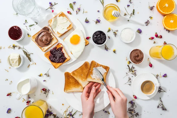 Vue recadrée d'une femme tenant un couteau tout en étalant du fromage à la crème sur du pain grillé savoureux sur blanc — Photo de stock