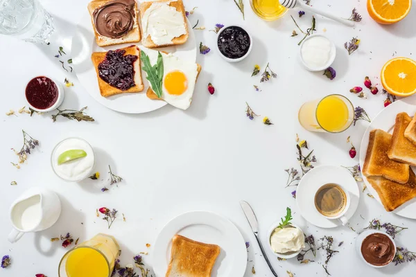 Top view of plates with tasty toasts near drinks and bowls with jam and chocolate cream on white — Stock Photo