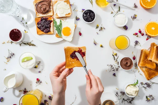 Vue recadrée d'une femme étalant de la crème au chocolat sur des toasts savoureux près de boissons sur blanc — Photo de stock