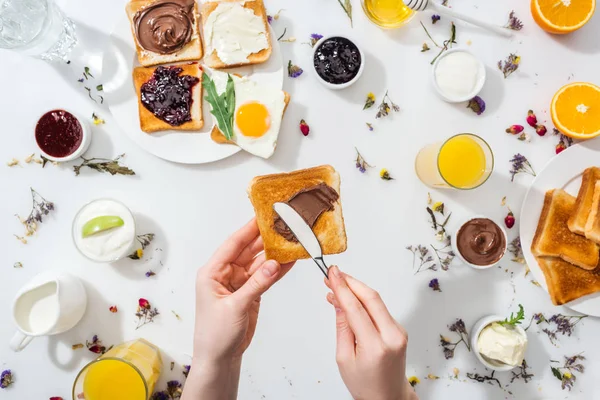 Cropped view of woman spreading chocolate cream on toast near drinks on white — Stock Photo