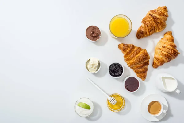 Top view of tasty croissants near bowls with jam and orange juice on white — Stock Photo