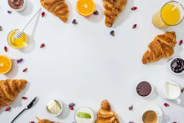 Vista superior de croissants saborosos perto de tigelas com engarrafamento, mel, laranjas e flores secas em branco — Fotografia de Stock