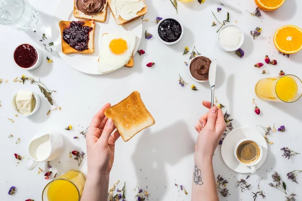 Cropped view of tattooed woman holding knife and toast in hands on white — Stock Photo