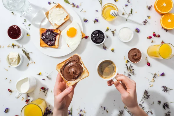 Abgeschnittene Ansicht einer Frau, die Toast mit Schokoladencreme und Tasse Espresso in der Nähe des Frühstücks auf weiß hält — Stockfoto