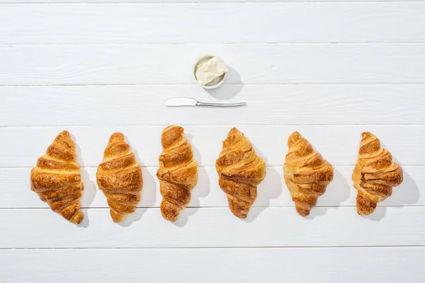 Vista superior da faca perto da tigela com queijo creme e croissants no branco — Fotografia de Stock