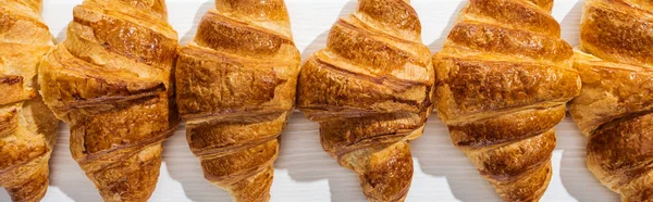 Plano panorámico de croissants dulces, sabrosos y frescos en la superficie blanca - foto de stock