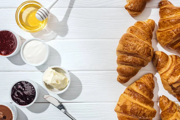 Top view of fresh croissants near bowls with cream cheese, chocolate cream, sour cream, jam and honey on white — Stock Photo